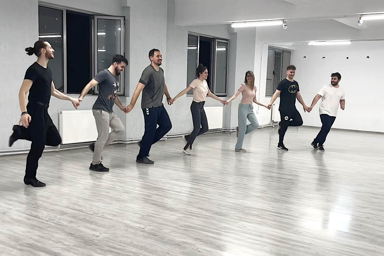 o imagine din sala bloomart academy cu grupa de la dans de societate adulti in timp ce danseaza un dans de grup, tinandu-se de mana in sir.